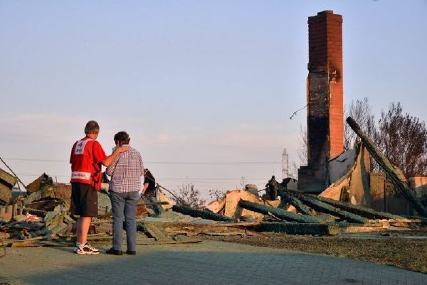 Red Cross volunteer comforting person in front of a destroyed home.