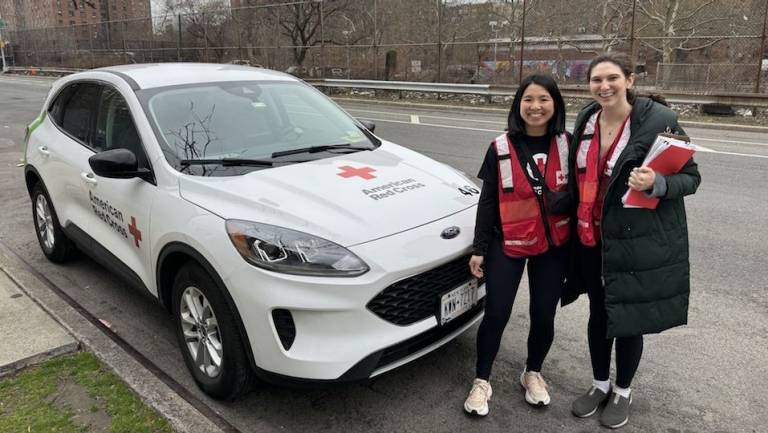 Two women in Red Cross red vests standing in front of a Red Cross vehicle