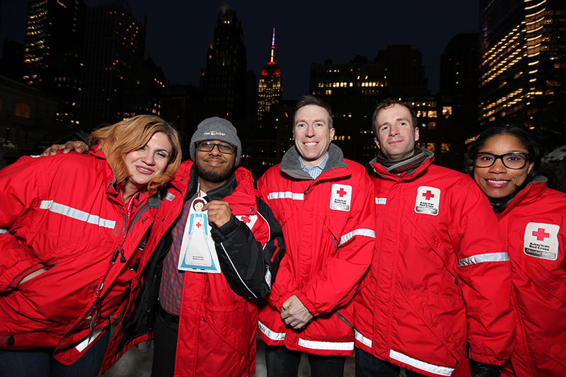 5 Red Cross volunteers below the New York City skyline smiling for the camera