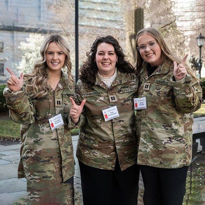 Three female Texas Tech Law students in military camo shirts smiling for camera