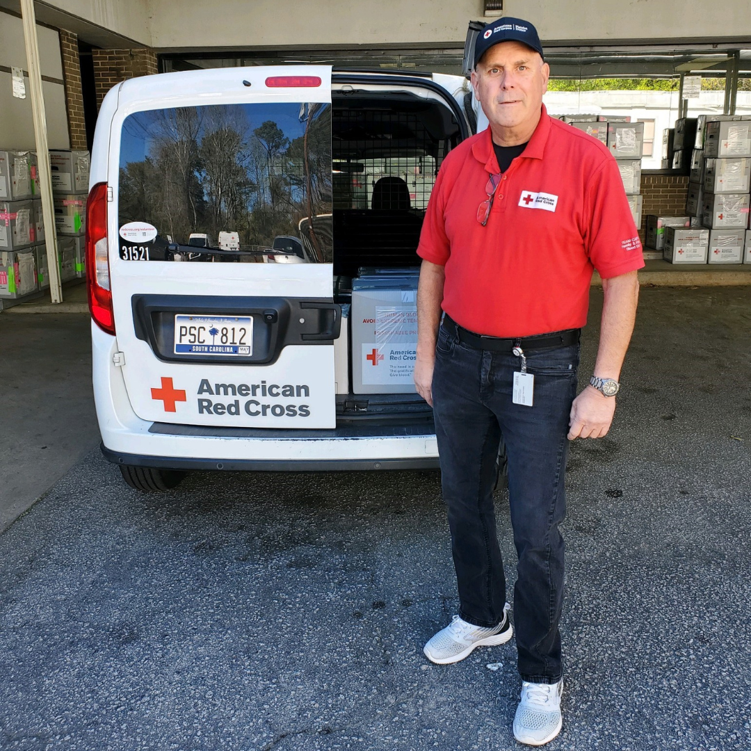 Blood Transportation Volunteer stands next to red cross van