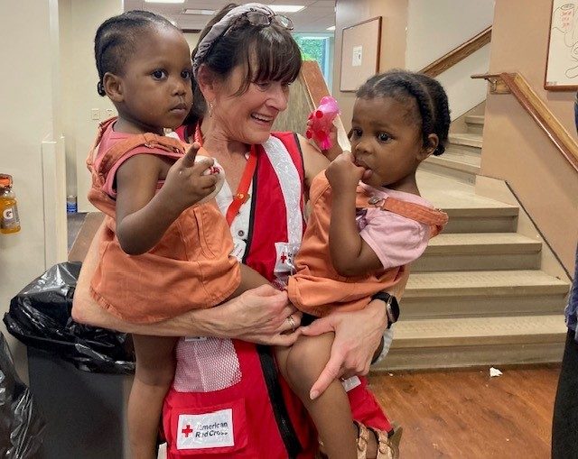 Red Cross volunteer holding two children in her arms