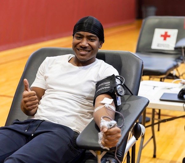 Smiling young man gives a thumbs up to the camera while donating blood.