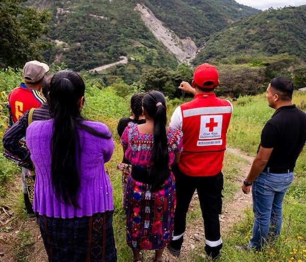 Local residents stand overlooking the countryside with members of the Red Cross to discuss disaster risks