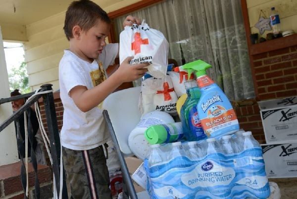 Young boy next to chair with cleaning supplies, paper plates, Red Cross bags and water bottles.
