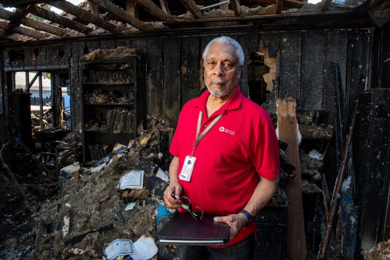 Red Cross volunteer with glasses and notebook in damaged home