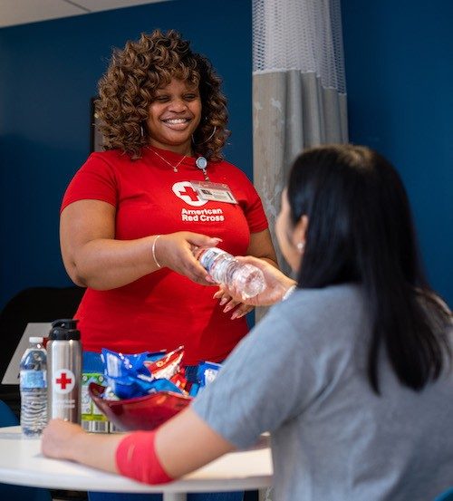 Red Cross volunteer handing water bottle to blood donor