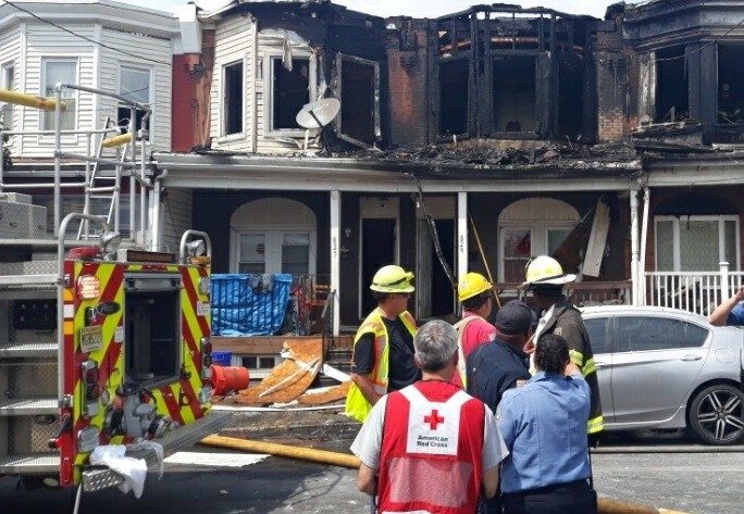 Burnt apartment building with fire fighters in front and a Red Cross volunteer in a Red Cross vest