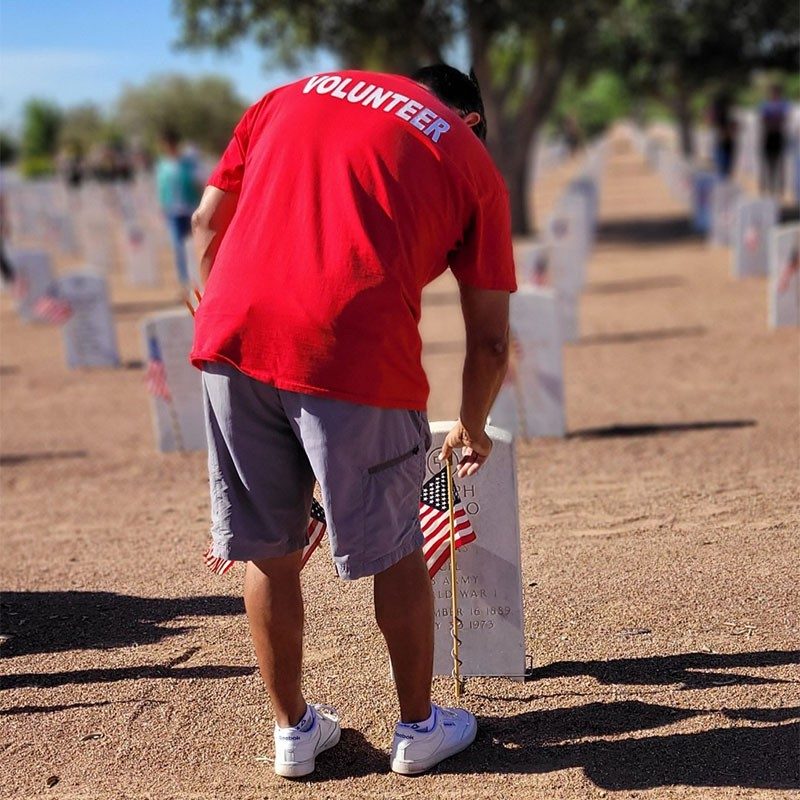 Red Cross volunteer putting American flag on veteran's grave.