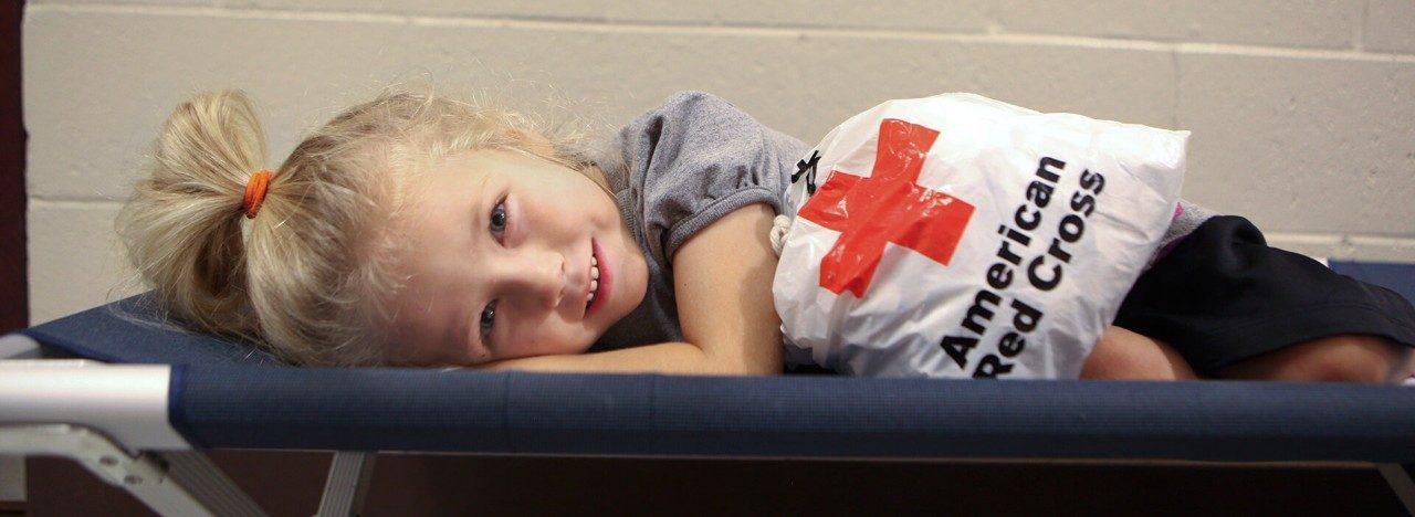 Yound child laying down next to Red Cross bag.
