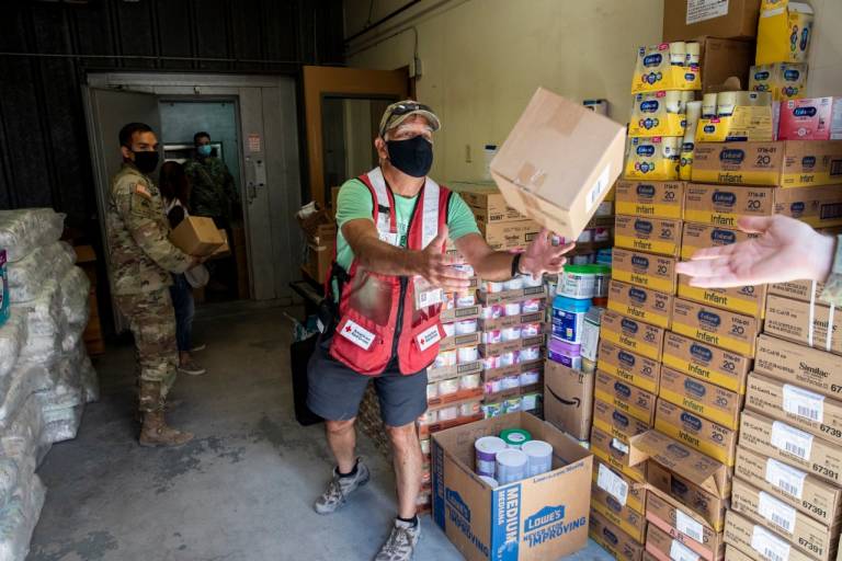 Red Cross volunteers work shoulder to shoulder with service members load a truck with much-needed supplies for Afghan evacuees.
