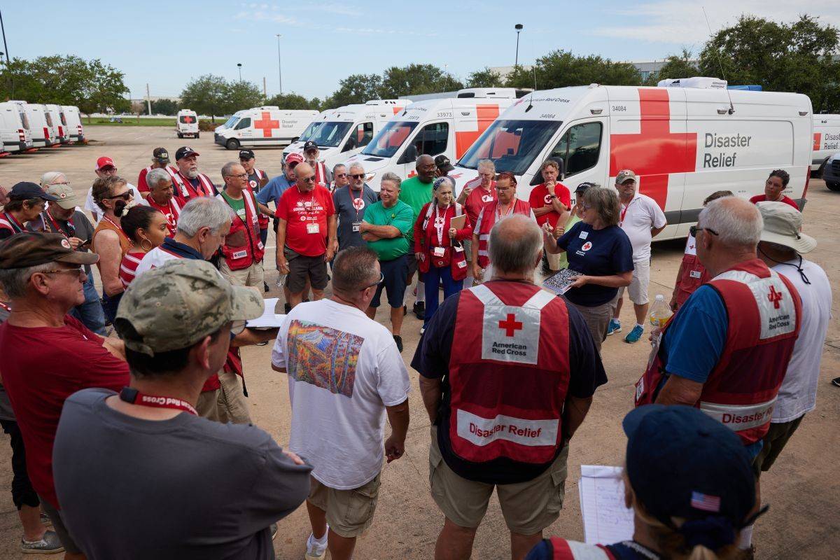 Dozens of Red Cross volunteers gather in a parking lot full of emergency response vehicles to coordinate the day's events