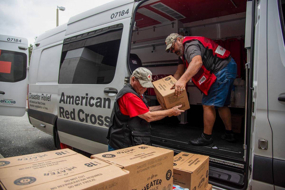 Two Red Cross volunteers are unloading disaster relief supplies from a Red Cross emergency vehicle