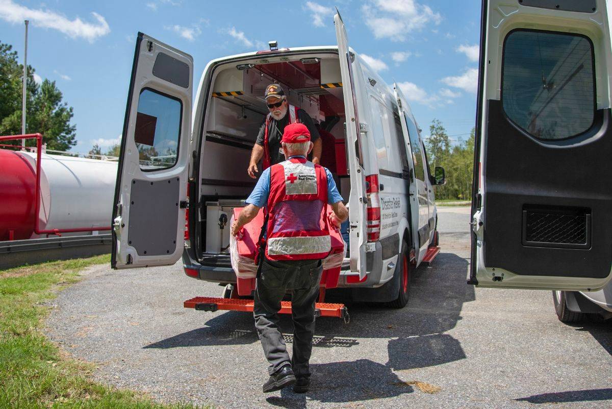 Two Red Cross volunteers are loading disaster relief supplies into the back of an emergency response vehicle