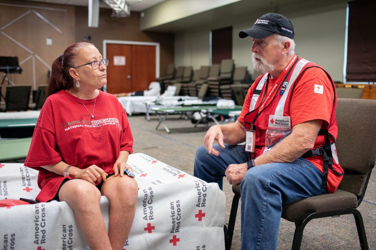 Red Cross volunteer sitting and talking with Tina Jackson in an American Red Cross shelter.