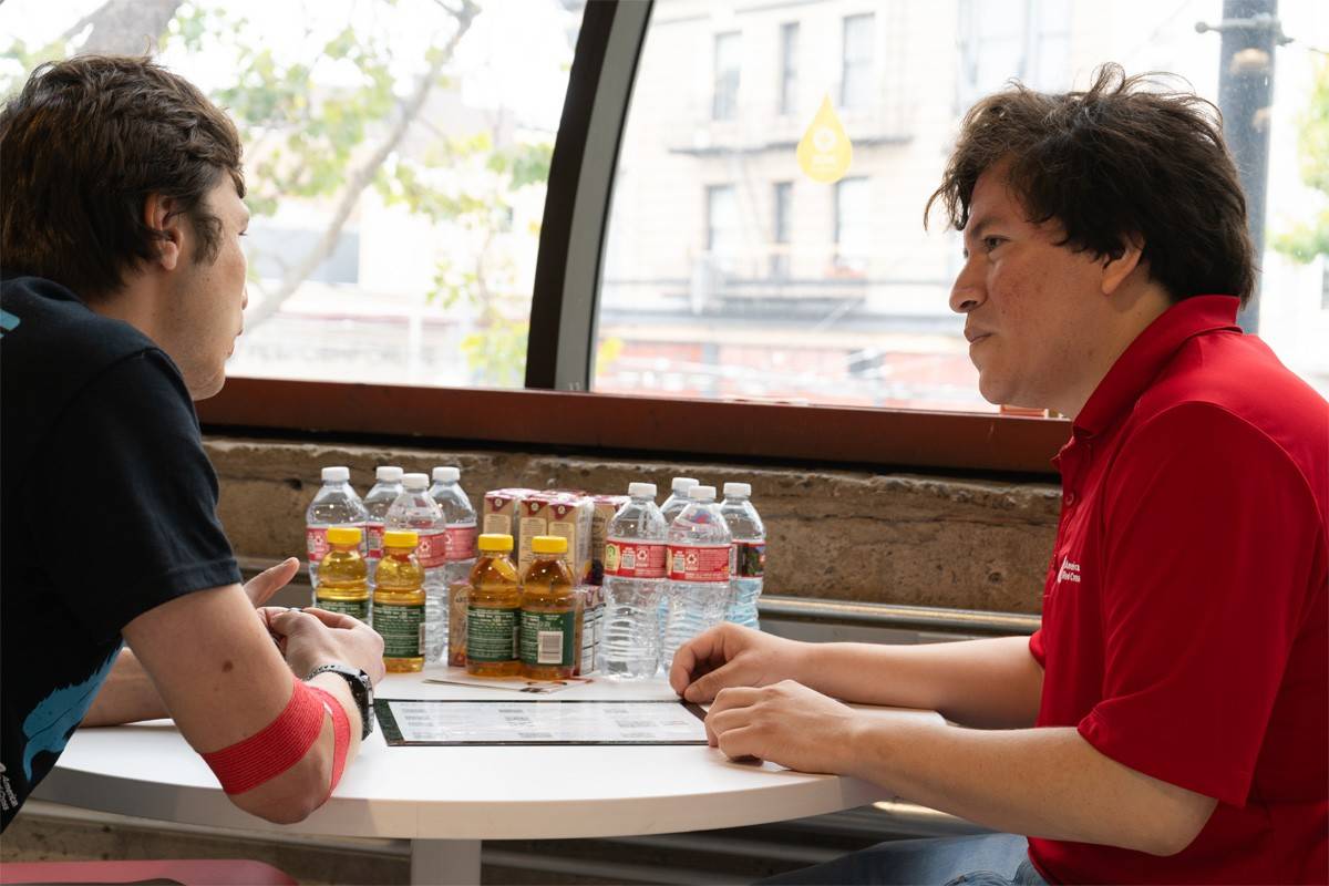 Alexander Clemente está sentado en una mesa hablando con un amigo después de donar sangre en un centro de donación de la Cruz Roja.