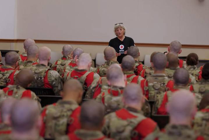 A Red Cross instructor is standing in front of a group of military service members explaining how the American Red Cross is there to help