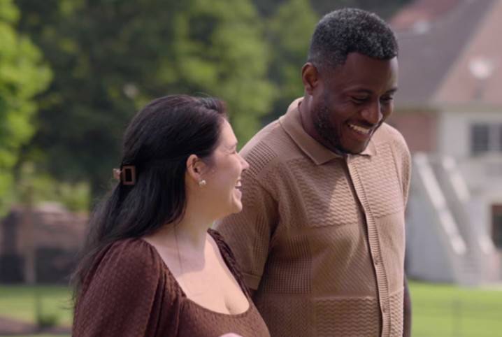 A man and a woman are walking across the front yard and they are smiling and laughing