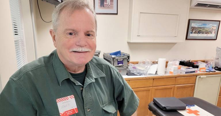 Mark Munson is standing inside a Red Cross blood donation site proudly smiling after donating blood