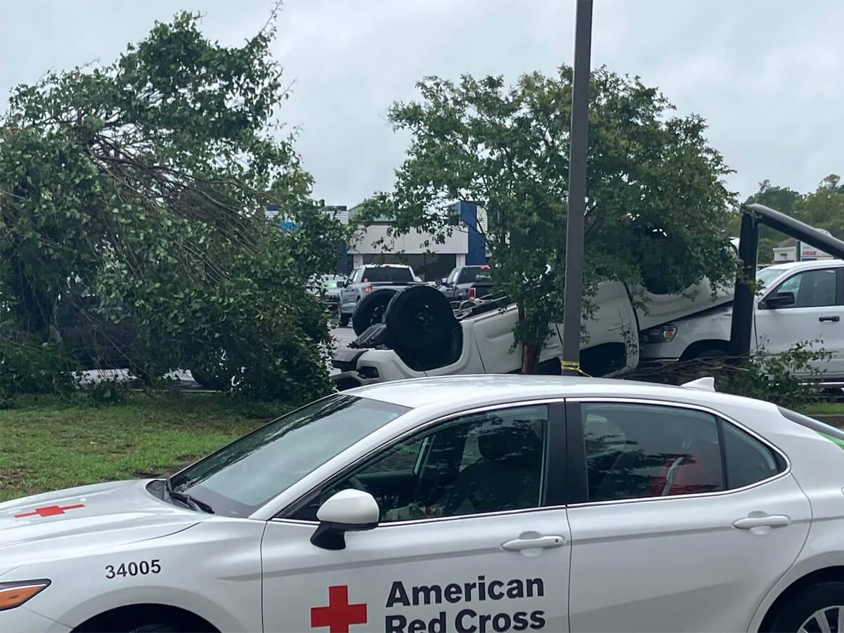 Several damaged vehicles in a store parking lot, one of them is upside down