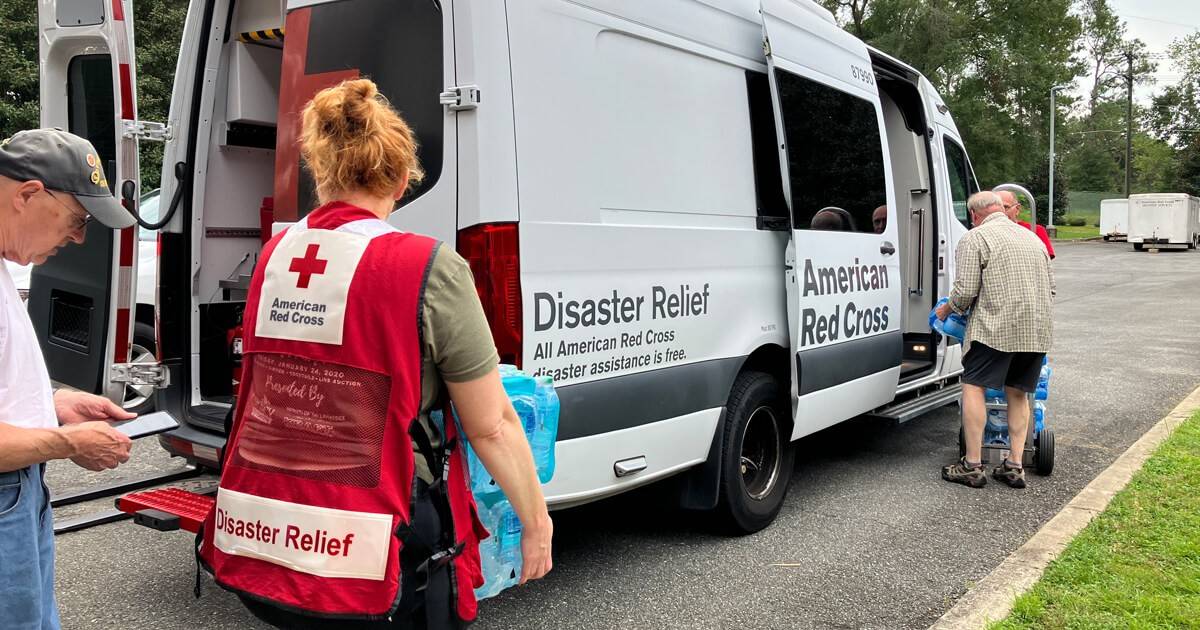 Several Red Cross volunteers are loading disaster relief supplies into the back of an emergency response vehicle