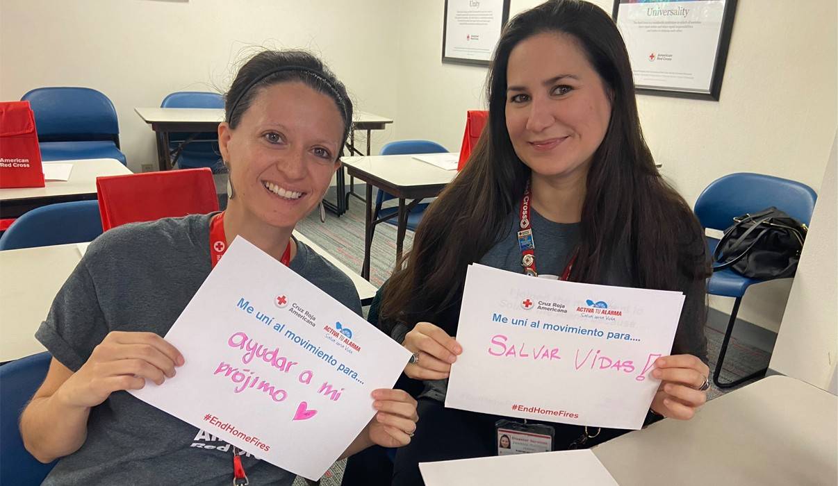 Voluntarias de Comunicaciones Multiculturales Luisa Torres Jessica Mairone sentadas en sus escritorios durante el entrenamiento de Activar la Alarma