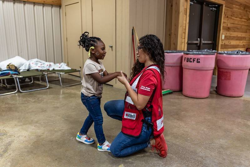 A Red Cross volunteer is playing with a young child at an emergency shelter