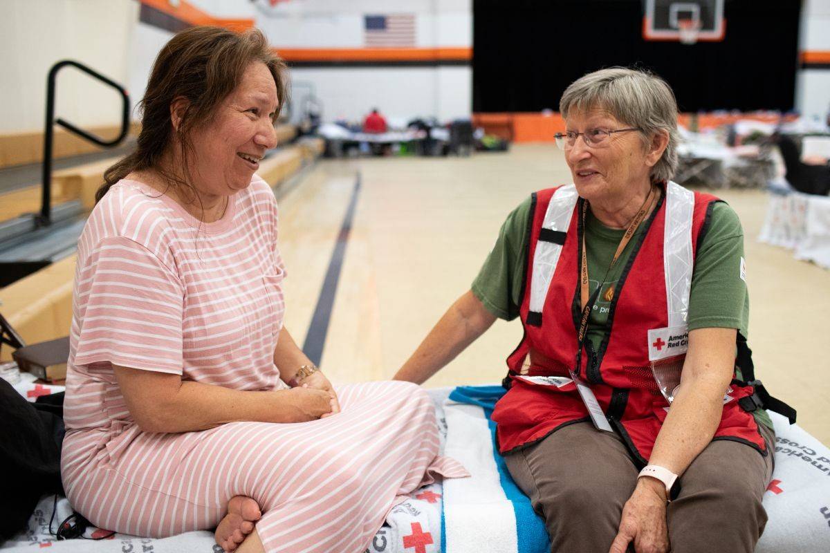 A photo of a woman speaking with a Red Cross volunteer at a shelter in a gymnasium