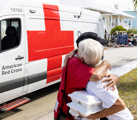 A Red Cross volunteer embraces a woman getting food from a Red Cross vehicle