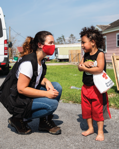 A Red Cross volunteer kneeling next to a young child.