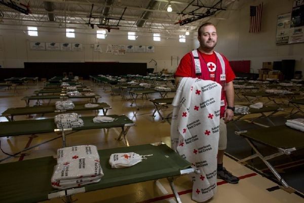 Red Cross volunteer carrying Red Cross blanket in shelter