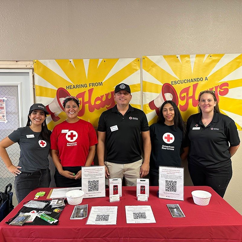 Group photo of American Red Cross volunteers at event with a table full of Red Cross promotional items.