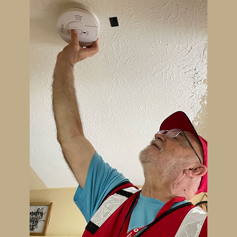 American Red Cross volunteer installing a smoke alarm on a ceiling.