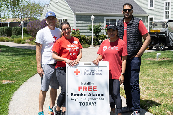 4 Red Cross volunteers standing next to a Red Cross FREE Smoke Alarms sign