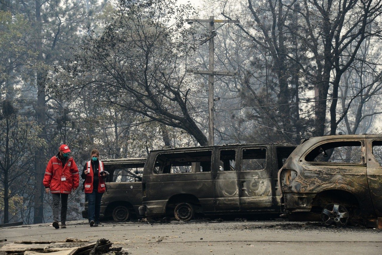 Two Red Cross volunteers walking by burnt vehicles from a forest fire.
