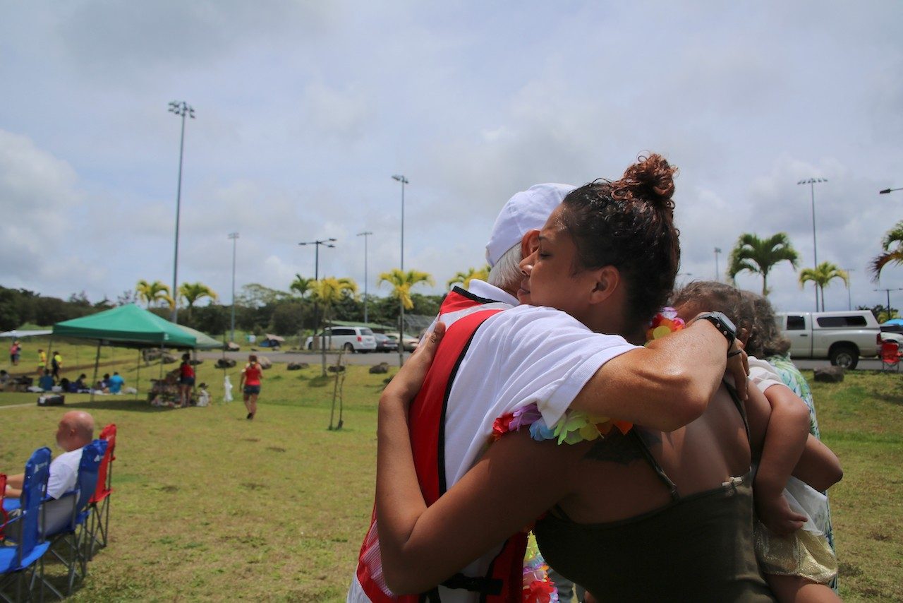 Red Cross volunteer hugging woman who's holding a child