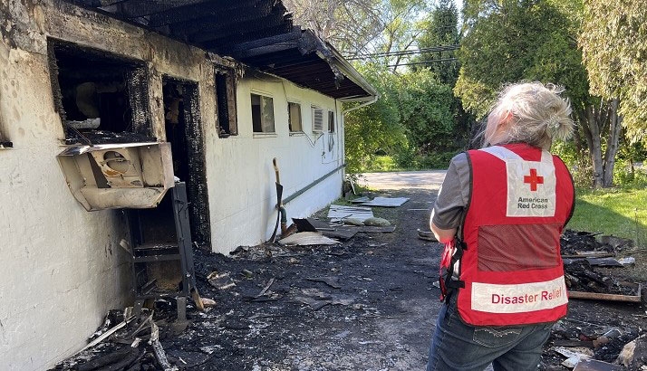 Red Cross volunteer standing next to burnt house.