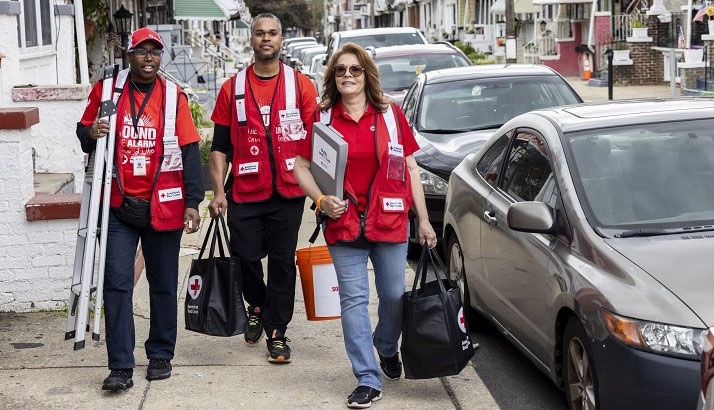 Red Cross volunteers walking on sidewalk with gear to install smoke alarms.