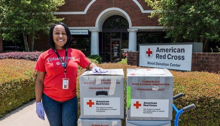 Red Cross volunteer standing next to cart of Red Cross blood boxes in front of American Red Cross blood donation center.