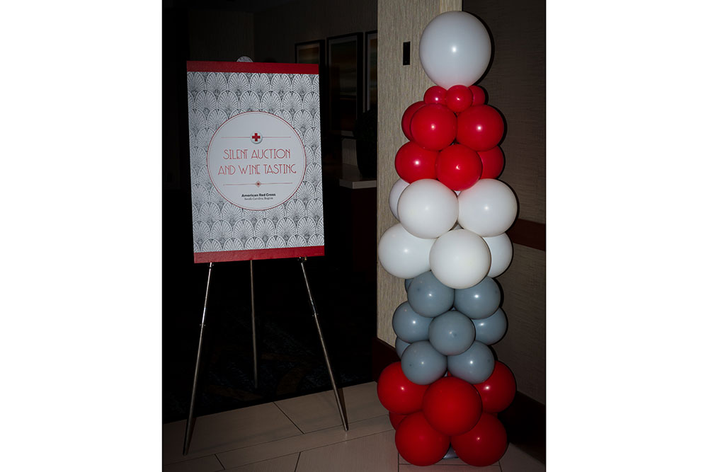 Silent auction and wine tasting sign next to red, white and gray balloons. 