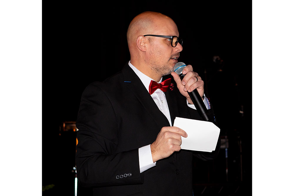 Person holding paper and speaking on a microphone at the Red Cross Gala.