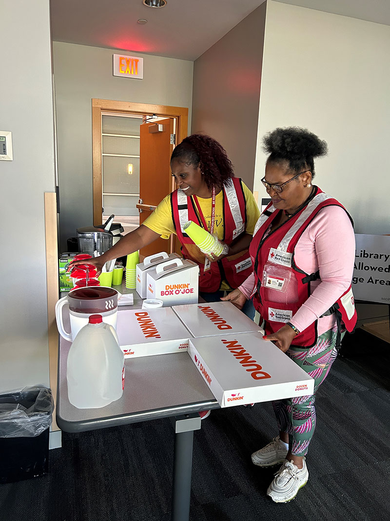 Two Red Cross volunteers setting up table with donuts and drinks