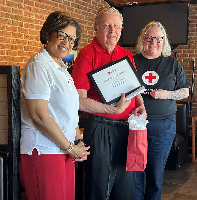 Three people standing next to each other with one holding Red Cross award