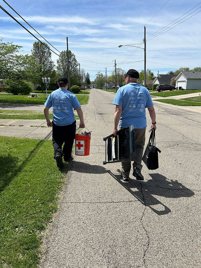 Two Red Coss volunteers walking on road hand carrying equipment