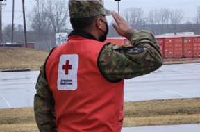 service member in uniform wearing a red cross vest saluting 