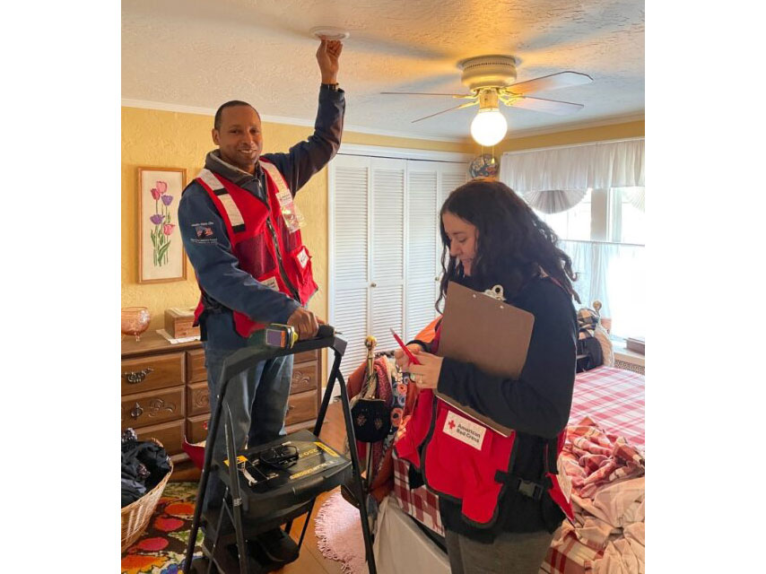 2 Red Cross volunteers installing a smoke alarm in house.