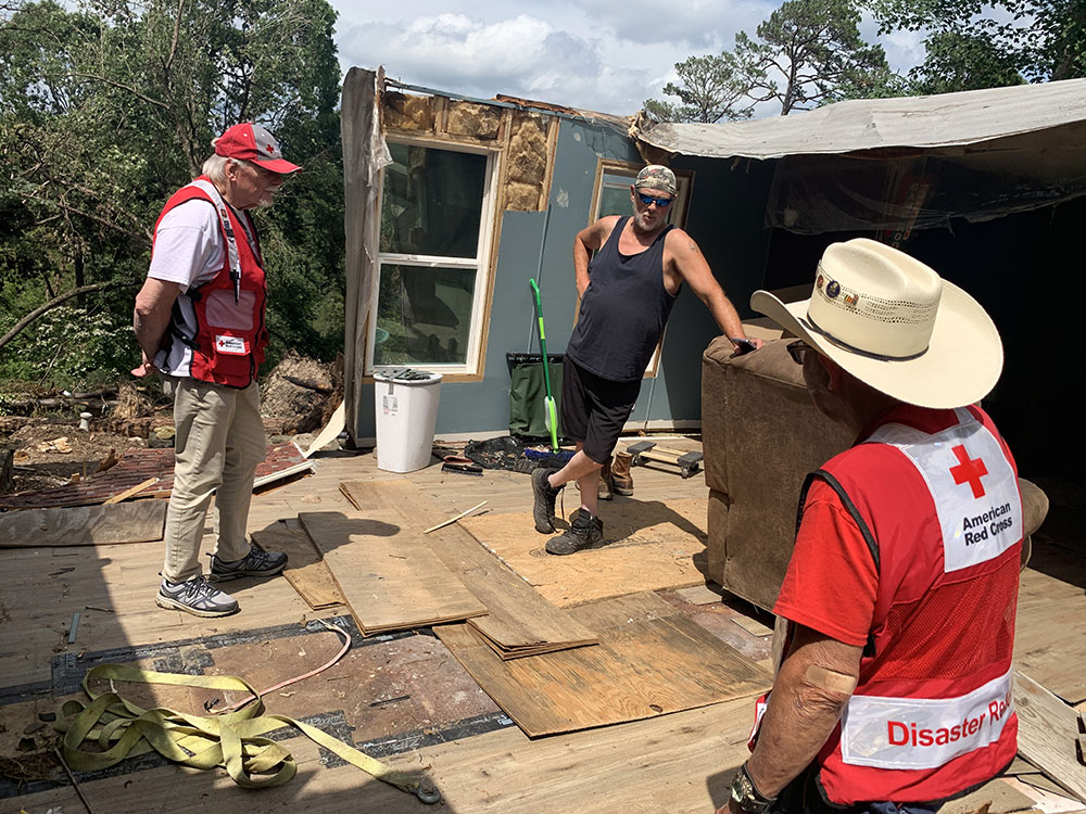 Two Red Cross volunteers talk with John Molz in demolished home