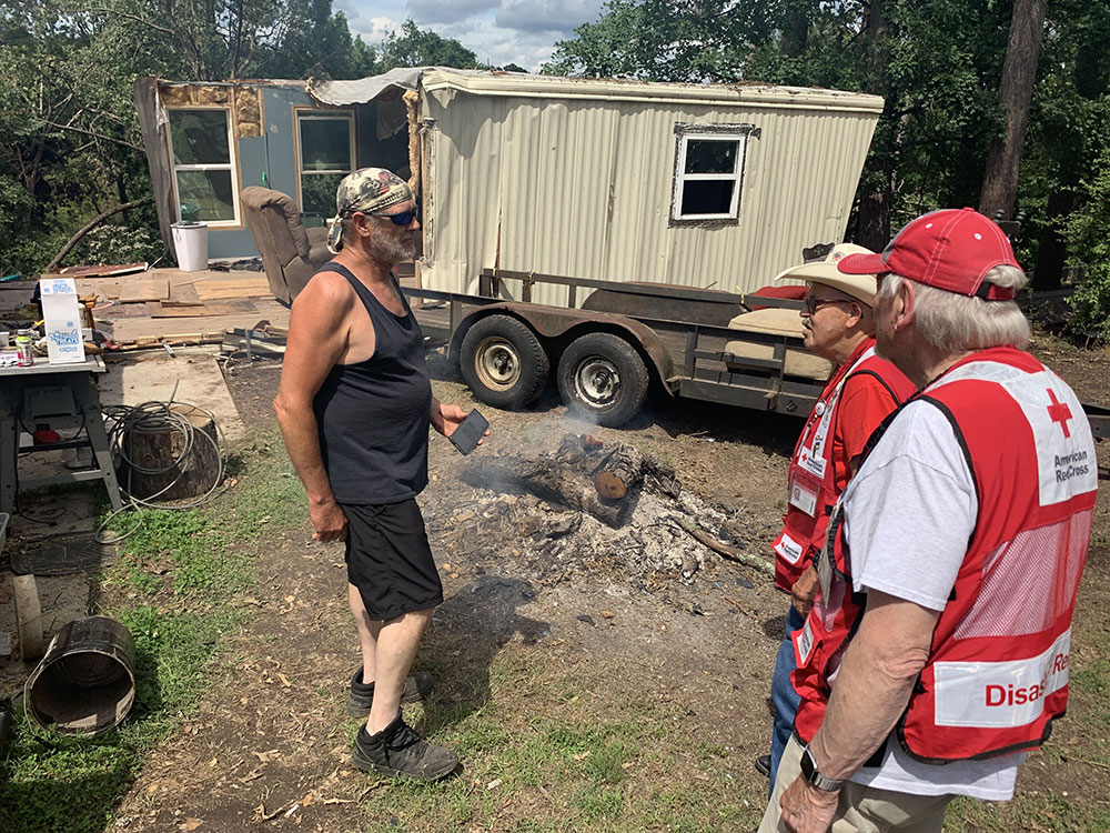 Two Red Cross volunteers talk with John Molz outside of demolished home