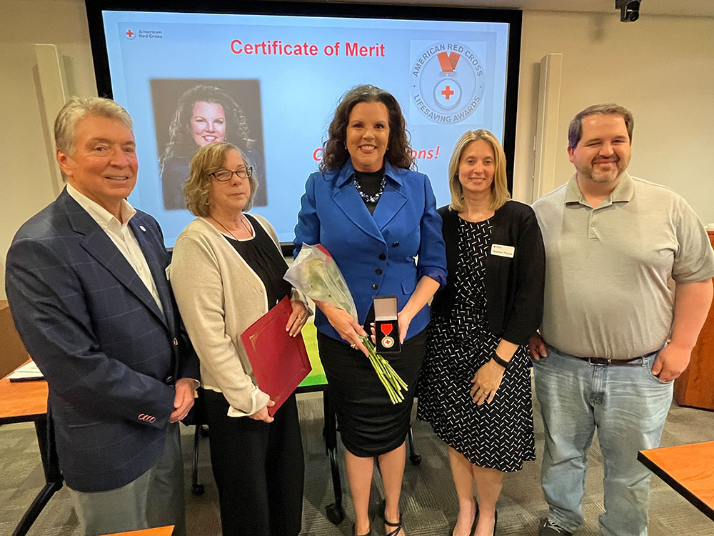 Lisa Fulk holding American Red Cross Certificate of Merit medal and flowers with a group of people next to her.