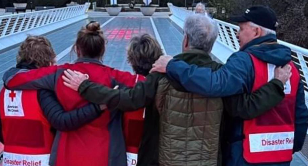 five red creoss volunteers hugging looking at sundail bridge 